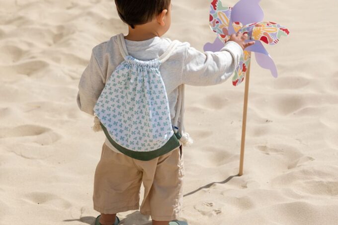 sac à dos Trèfles sur le dos d'un petit garçon sur le sable qui joue à un moulin à vent