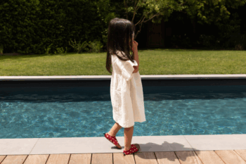 Chaussons souples rouges au motifs coquelicots aux pieds d'une petite fille au bord d'une piscine
